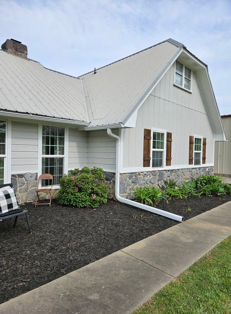 Light gray house with stone foundation, white trim, brown shutters, and black mulch landscaping.