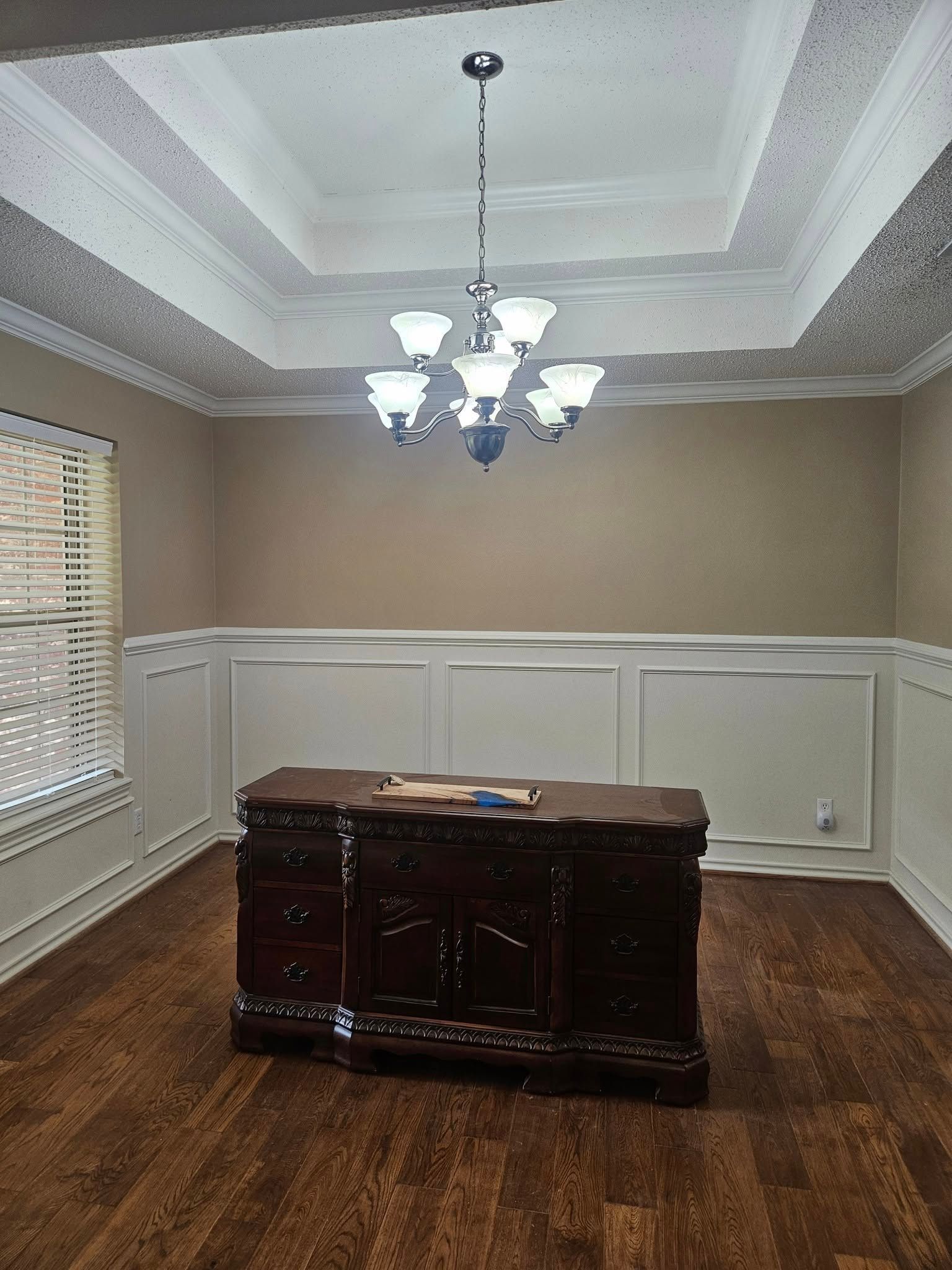 Formal dining room with dark wood buffet, chandelier, wood floors, and wainscoting.