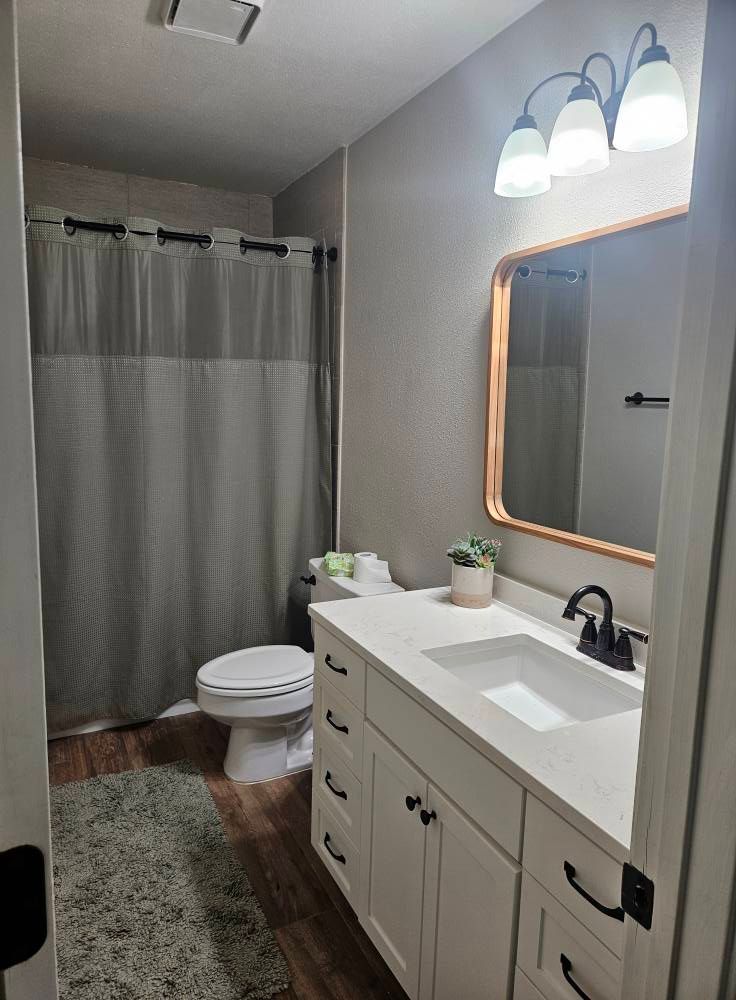 Bathroom with white vanity, gray walls, shower curtain, and a wooden floor.