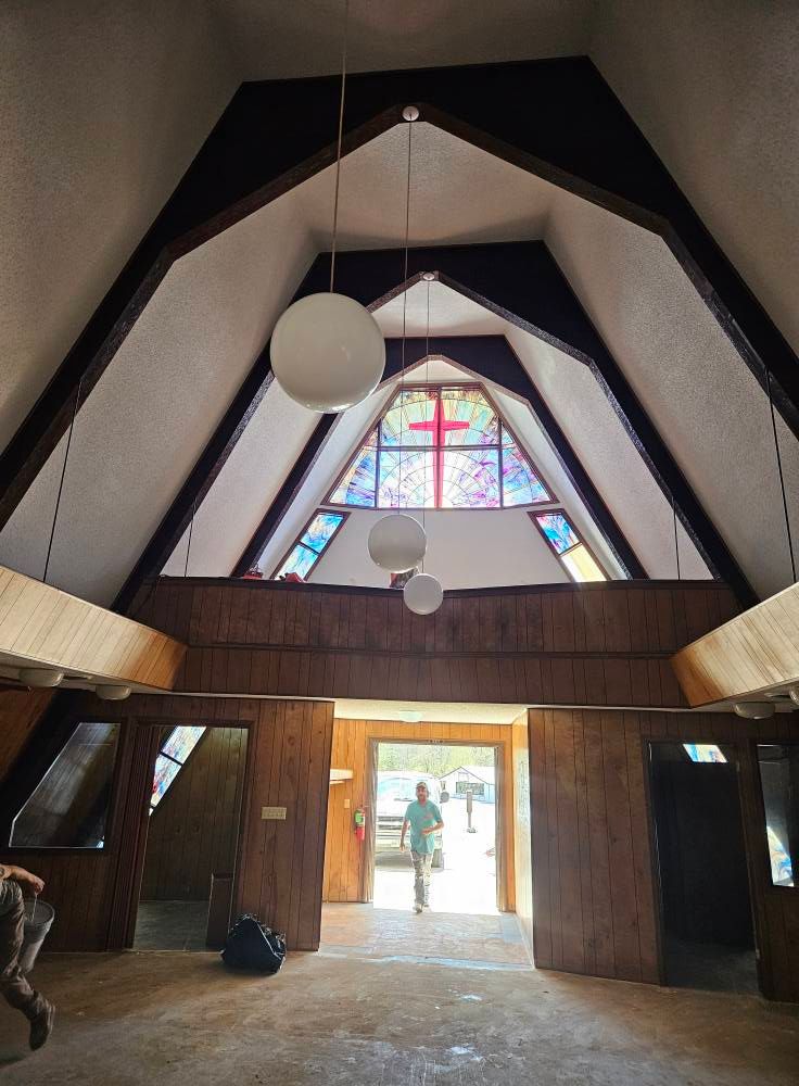 Interior of a building with a peaked ceiling, stained glass, and a person walking towards the open door.