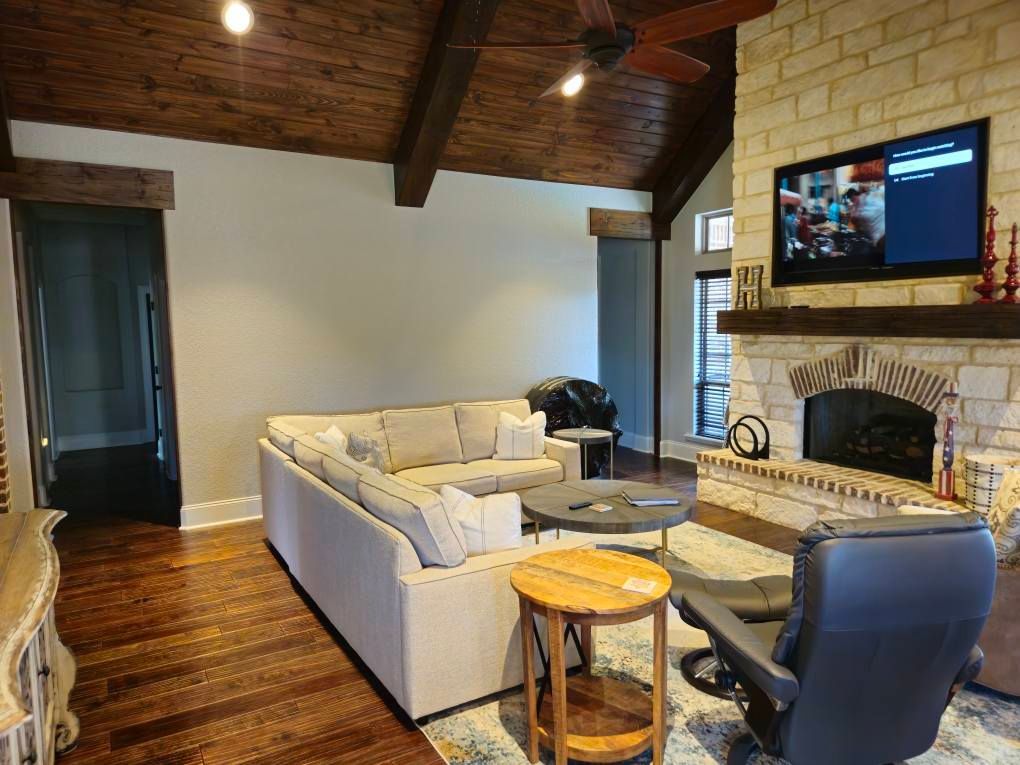 Living room with cream sectional, brick fireplace, TV, and wooden ceiling beams.