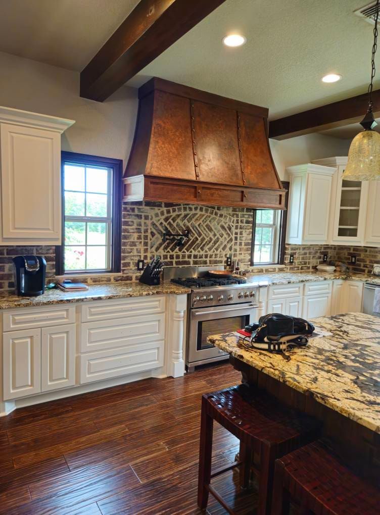 Kitchen with white cabinets, copper range hood, and brick backsplash.