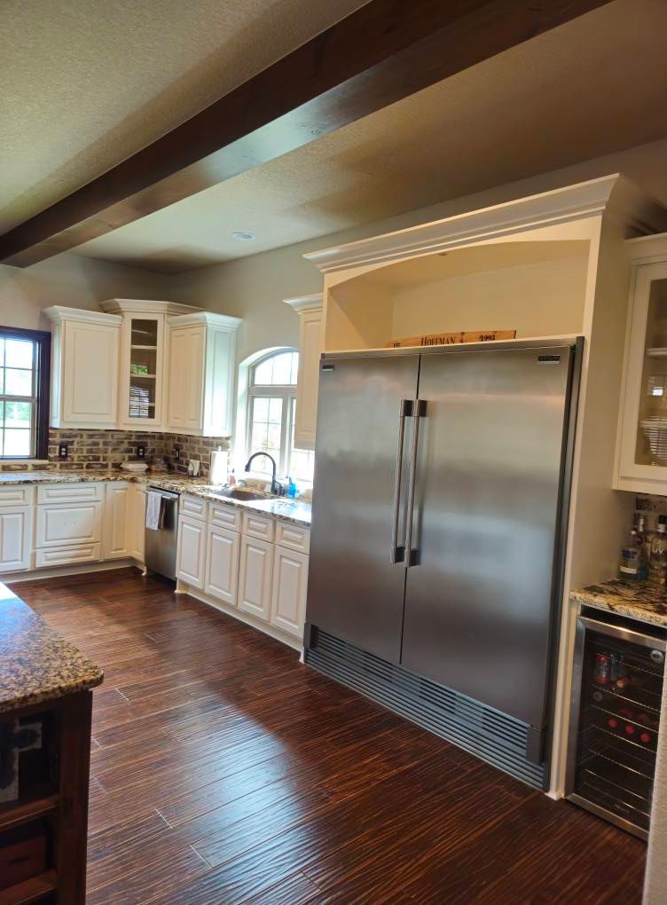 Kitchen with stainless steel refrigerator, white cabinets, dark wood floors, and wooden beams.