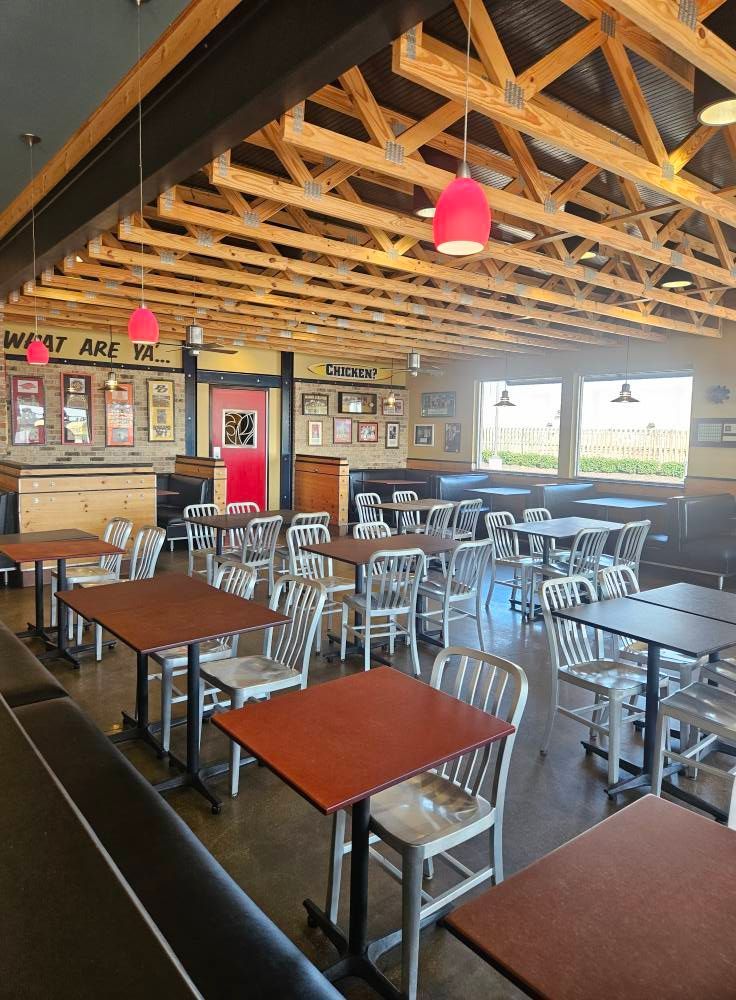 Restaurant interior with tables, chairs, and wooden ceiling beams; red pendant lights.
