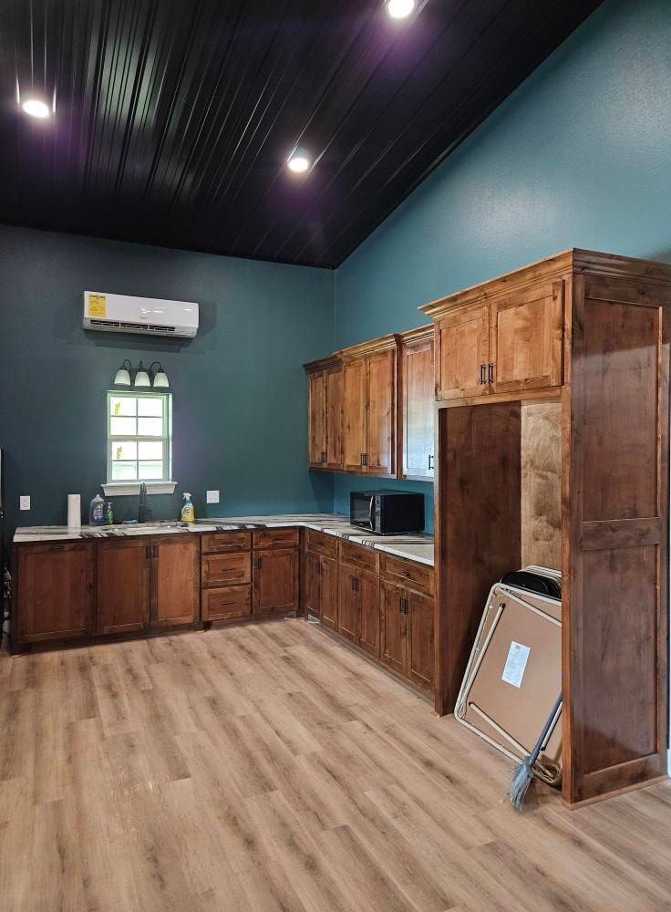 Kitchen with wood cabinets, teal walls, black ceiling, and light wood flooring.