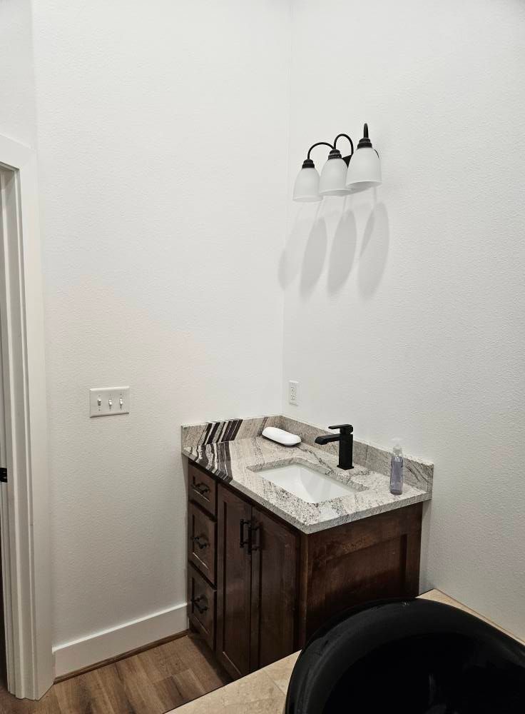 Bathroom with dark wood vanity, granite countertop, white sink, and black faucet.