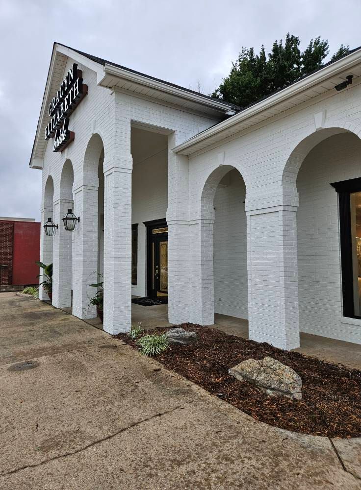 White-painted building with arched entryway, black door, and landscaping, possibly a business.