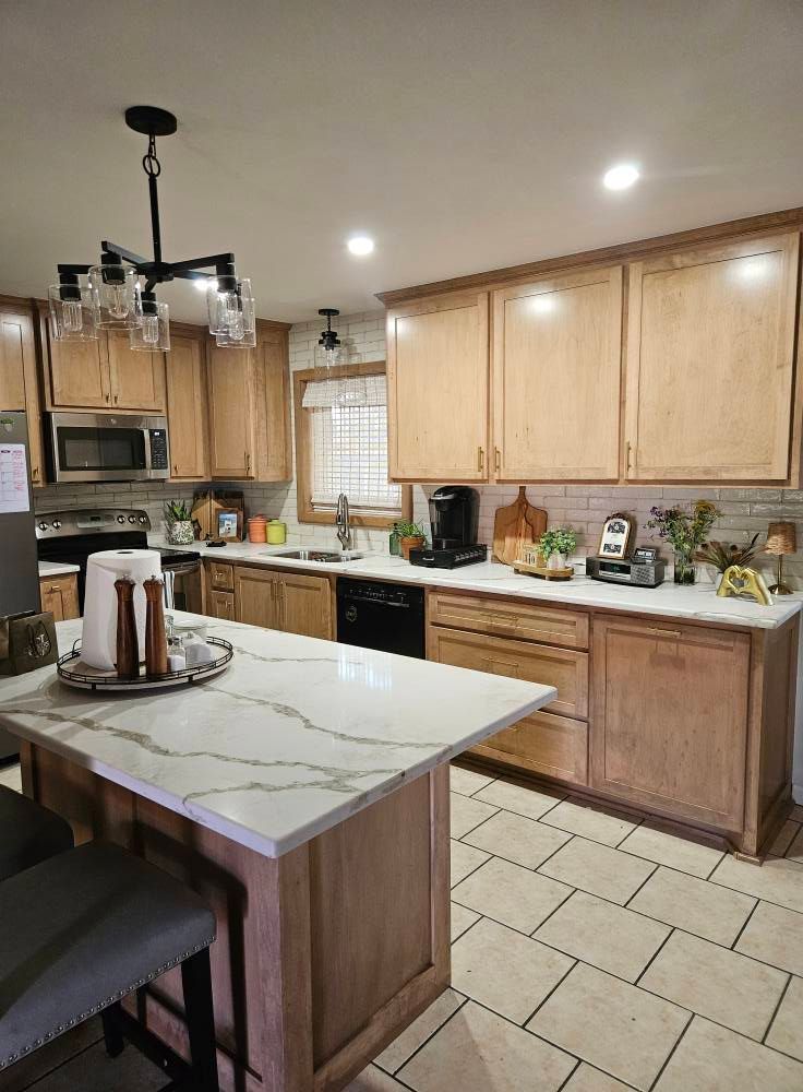 Kitchen with light wood cabinets, white countertops, island with seating, and black appliances.