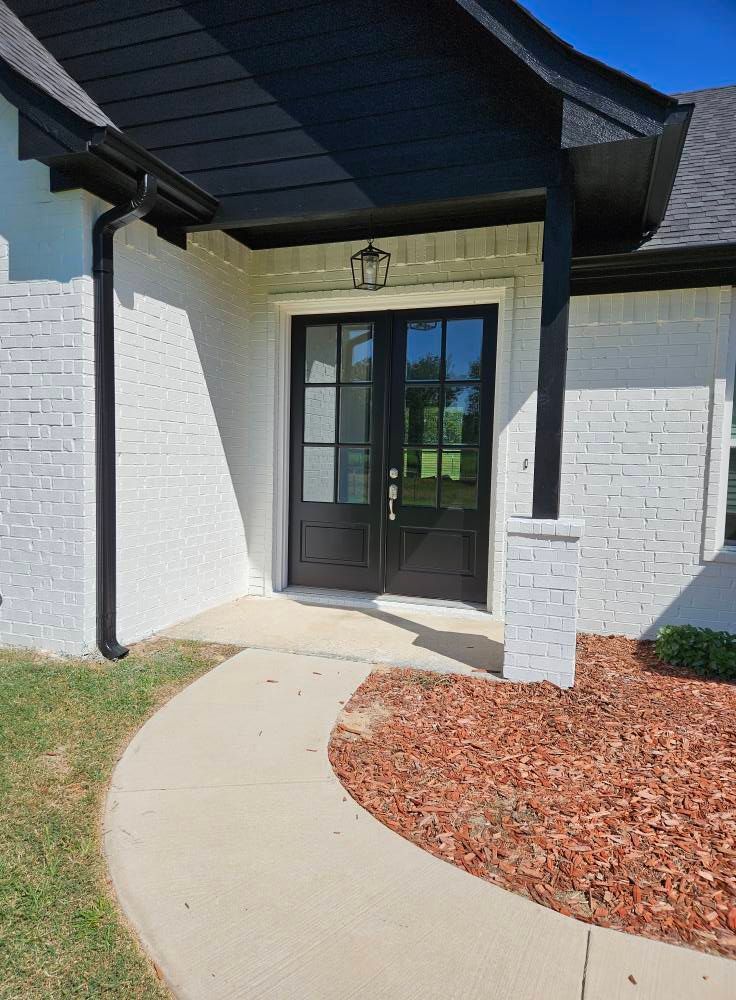 White brick house with black trim, double glass doors, and a winding walkway.