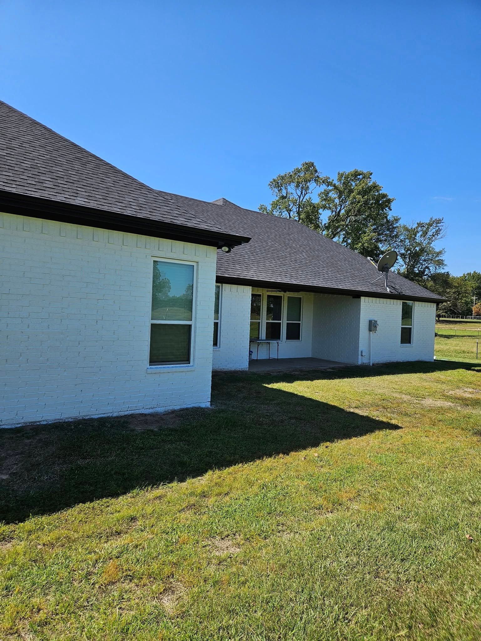 White brick house with dark roof and windows, set against a blue sky, grassy yard.