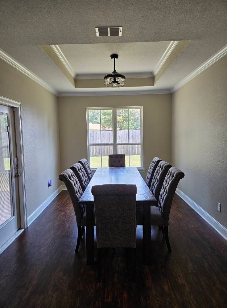 Dining room with long table, eight chairs, a window, and a hanging light fixture. Dark wood floors.