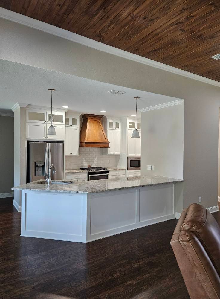 Kitchen with white cabinets, wood range hood, granite countertops, and wood ceiling.