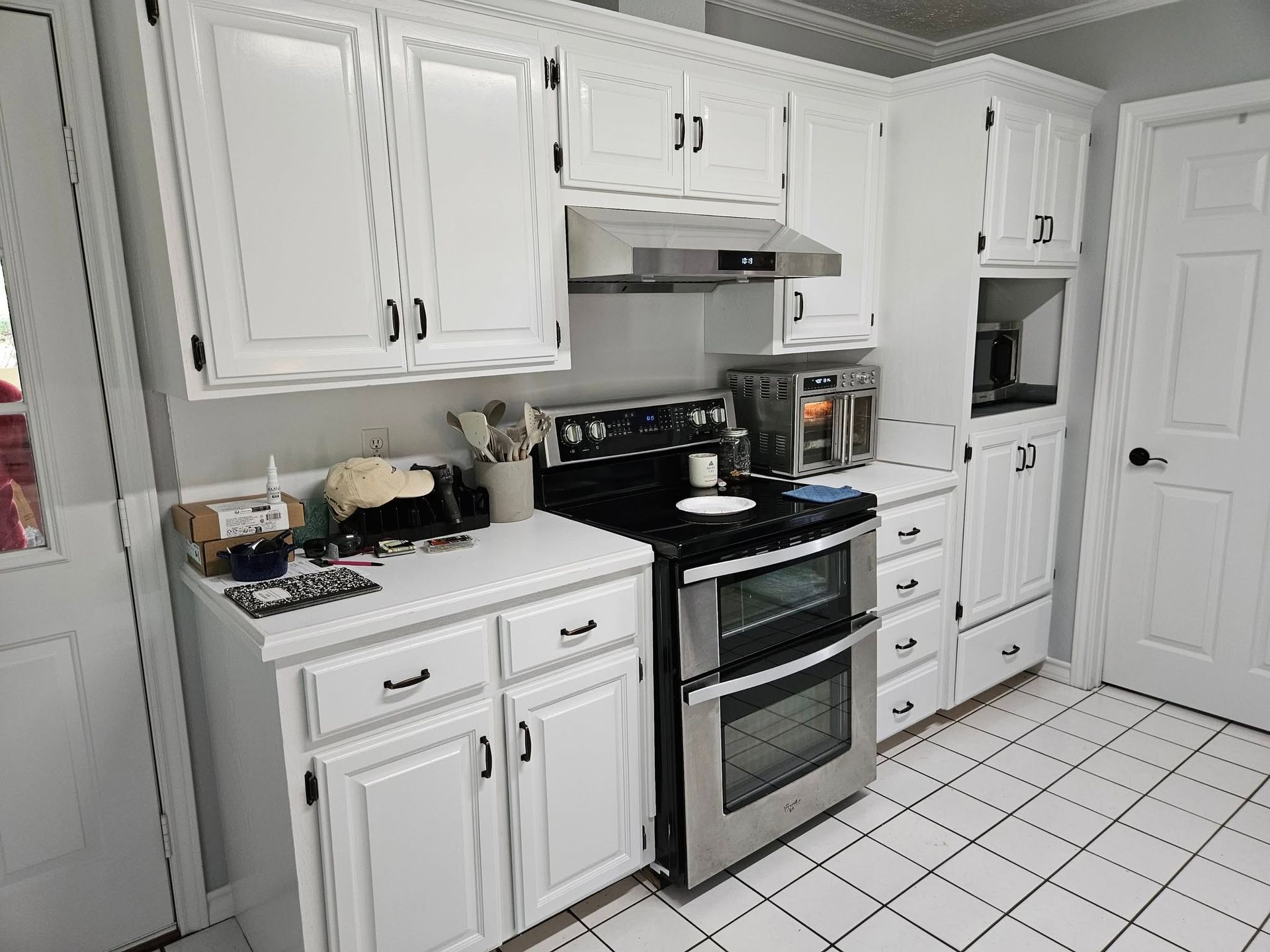 White kitchen with white cabinets, stainless steel oven, and white tile floor.