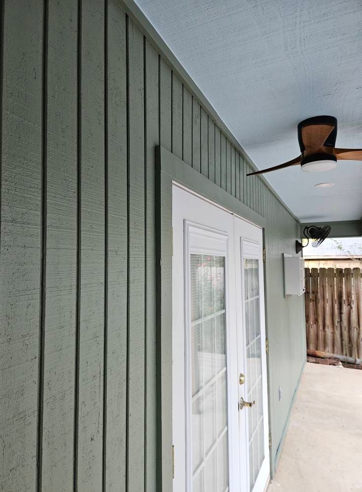 Green siding and blue ceiling with white double doors and a ceiling fan.