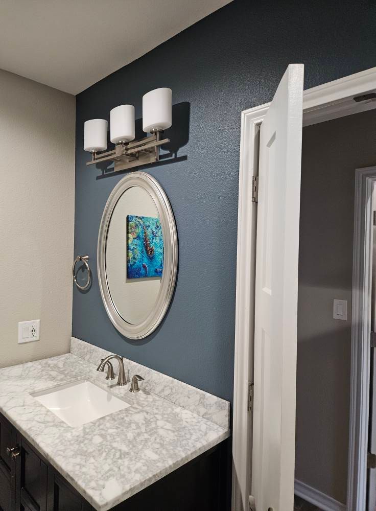 Bathroom with a blue accent wall, a silver-framed mirror, and a vanity with a white countertop.