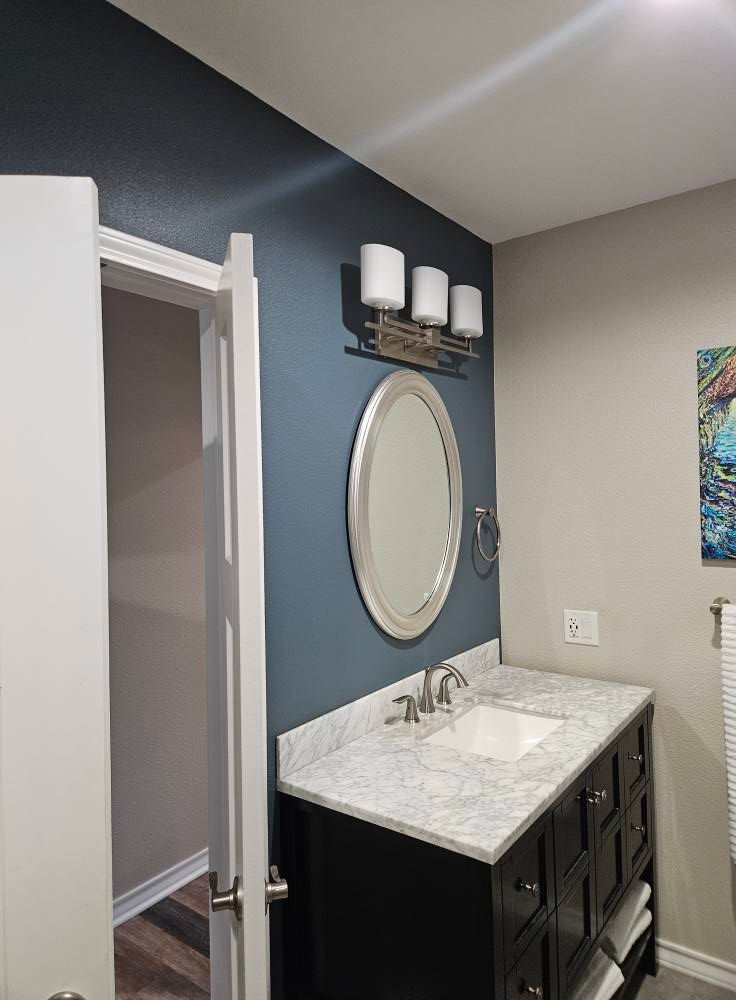 Bathroom with a dark blue accent wall, a silver-framed mirror, and a black vanity with a white countertop.