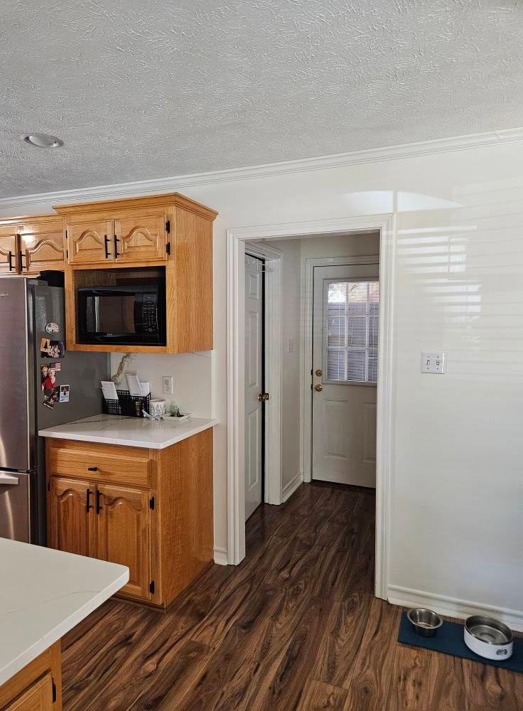 Kitchen with wood cabinets and flooring, stainless steel appliances, and a hallway leading to a door with a glass block window.