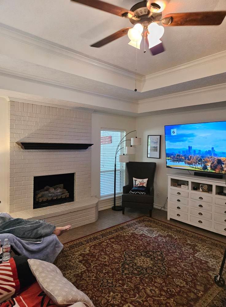 Living room with white brick fireplace, TV, rug, and ceiling fan.