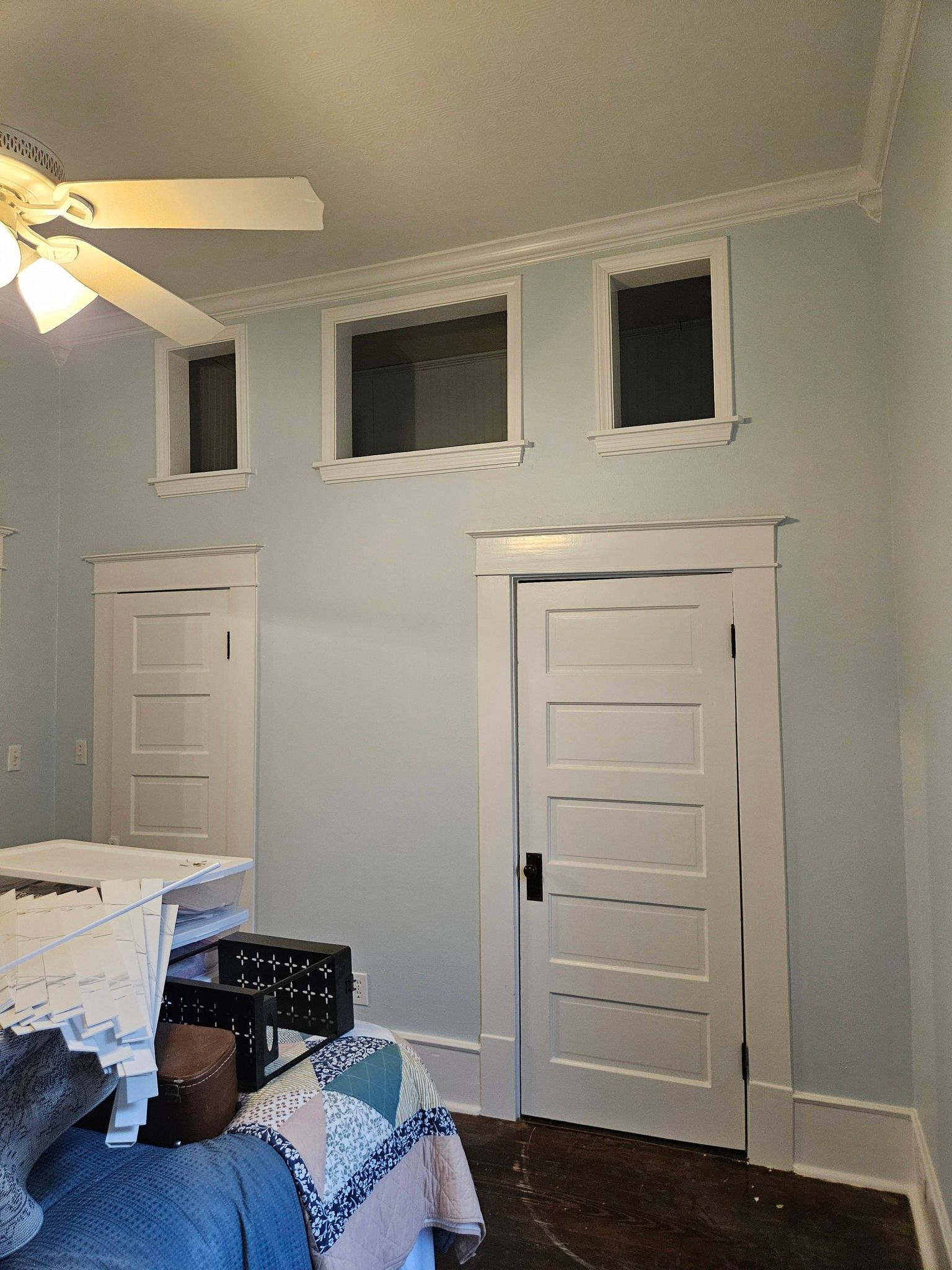 Room with light blue walls, white trim, and doors. Ceiling has crown molding and small windows.