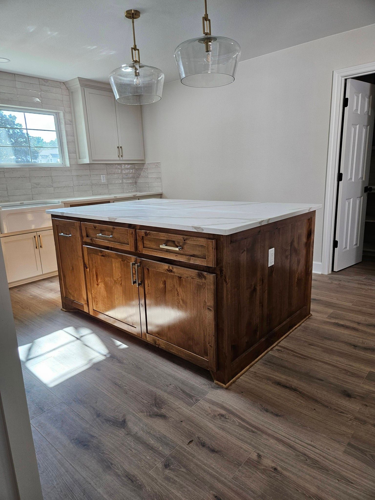 Kitchen with a wooden island, marble countertop, pendant lights, and wooden cabinets.