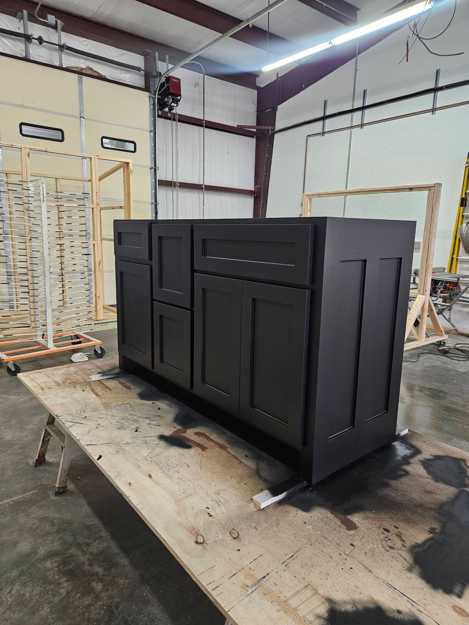 Black bathroom vanity cabinet on a wooden workbench in a workshop.
