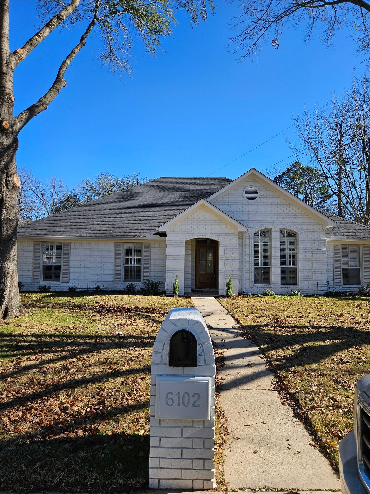 White brick house with mailbox, path, and bare trees under a clear blue sky.