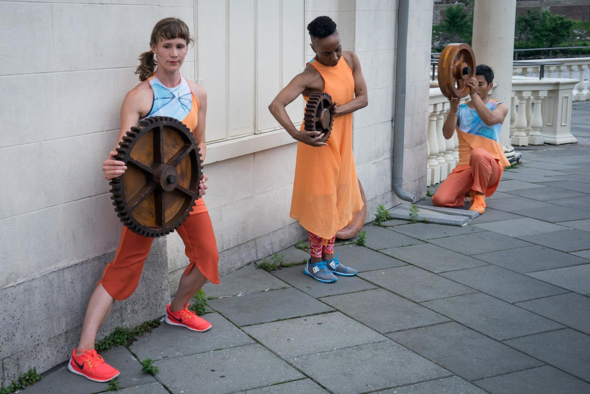 Three people are standing next to each other on a sidewalk holding objects.