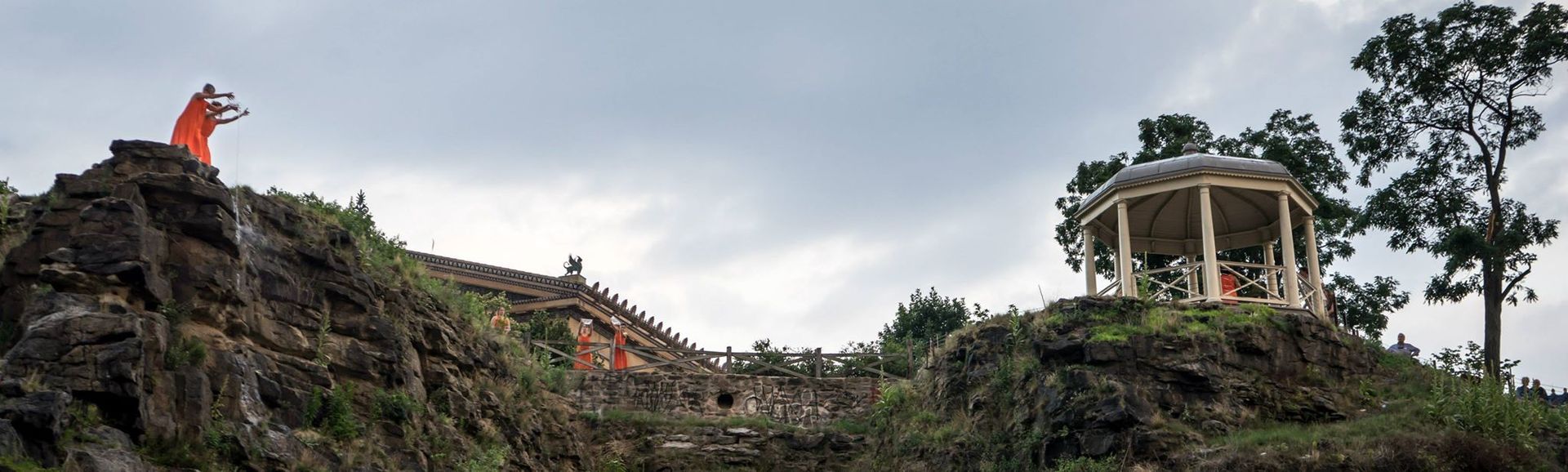 A man is standing on top of a rocky hill next to a gazebo.