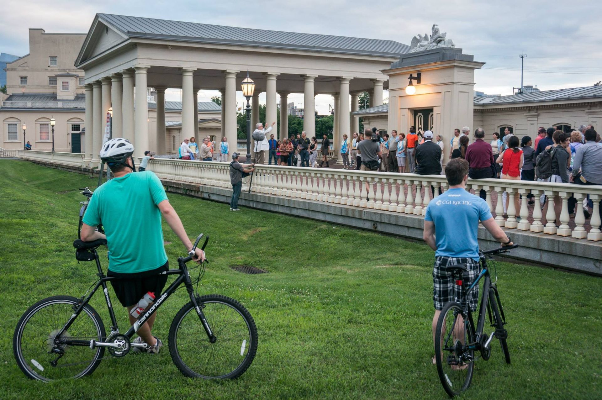 Two men are riding bicycles in front of a large building.