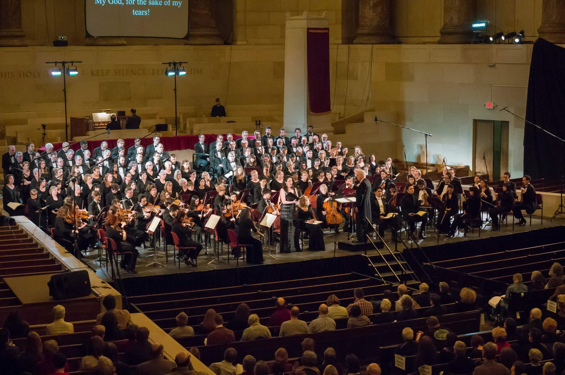 A large choir and orchestra are performing in a large auditorium