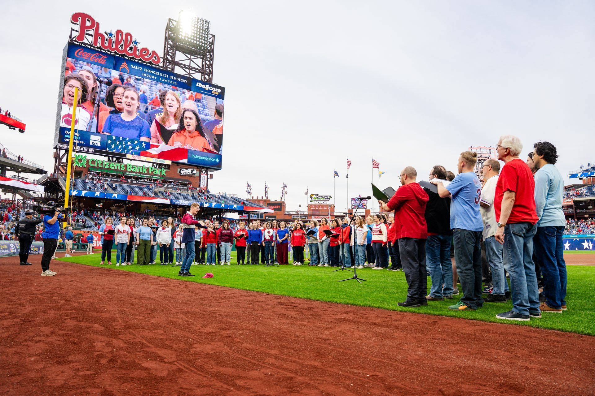 Audience watches a band and choir perform on stage, American flag in the background, red and white colors.