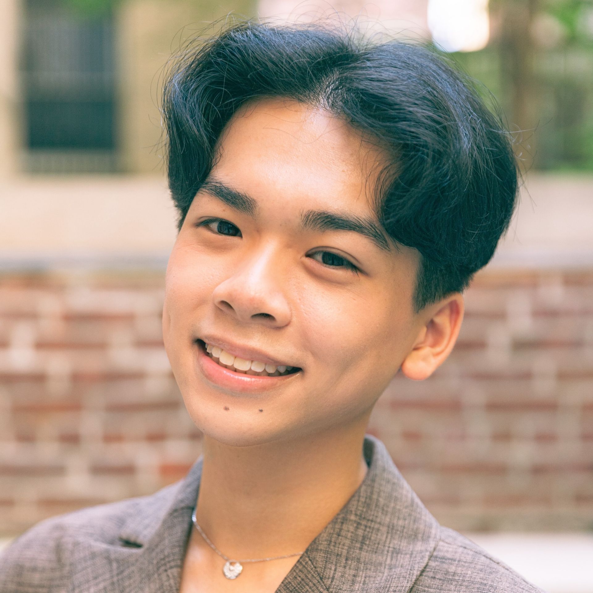Young Asian man smiles, wearing a black button-down shirt, standing in front of a YoungArts and Anthropologie backdrop.