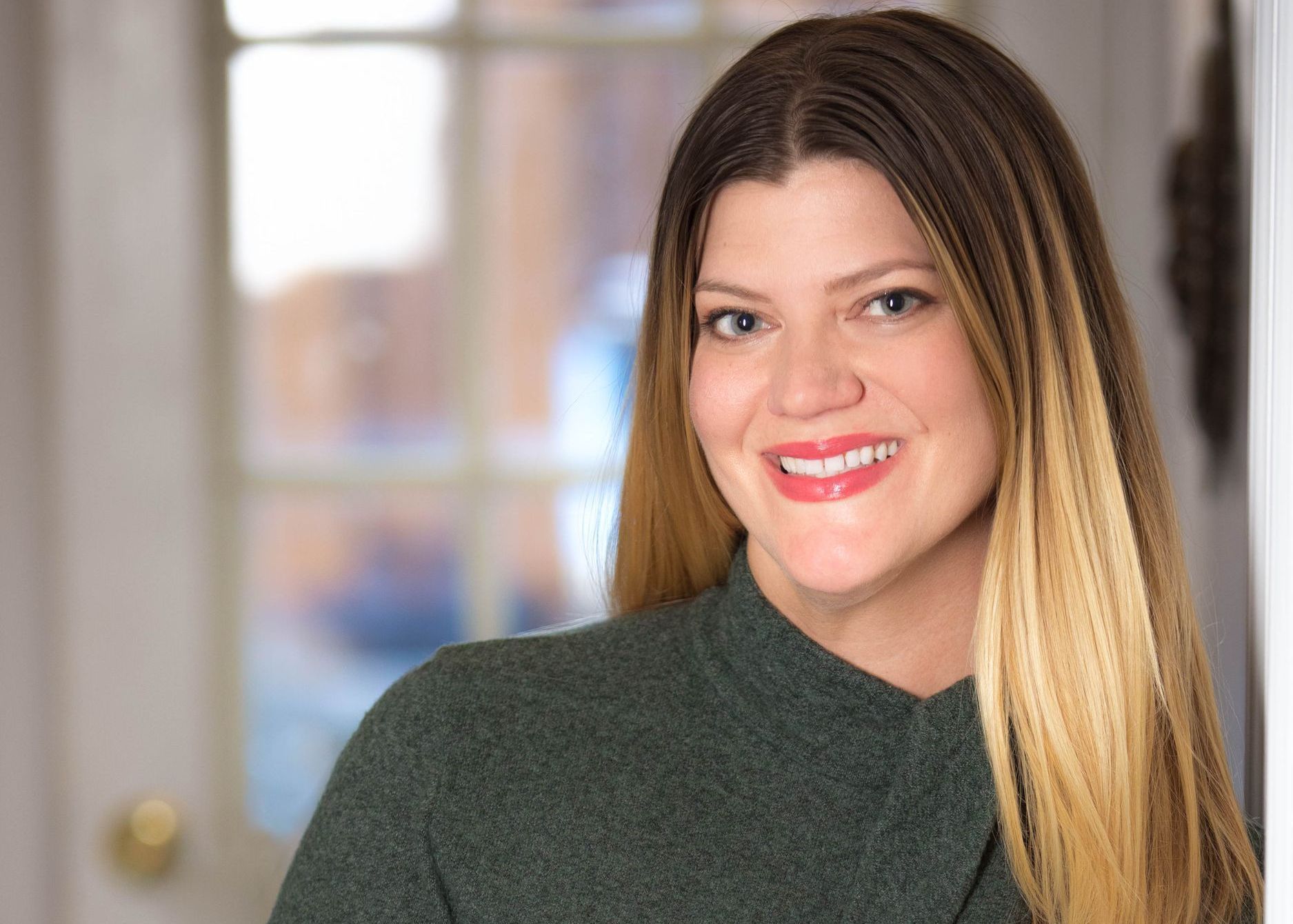 A woman in a green sweater is smiling for the camera.