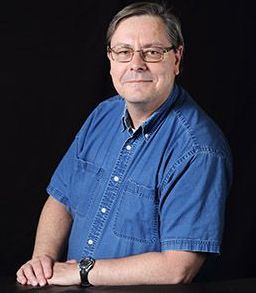 A man wearing glasses and a blue shirt is sitting at a table.