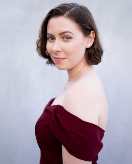 A woman in a red off the shoulder dress is looking at the camera