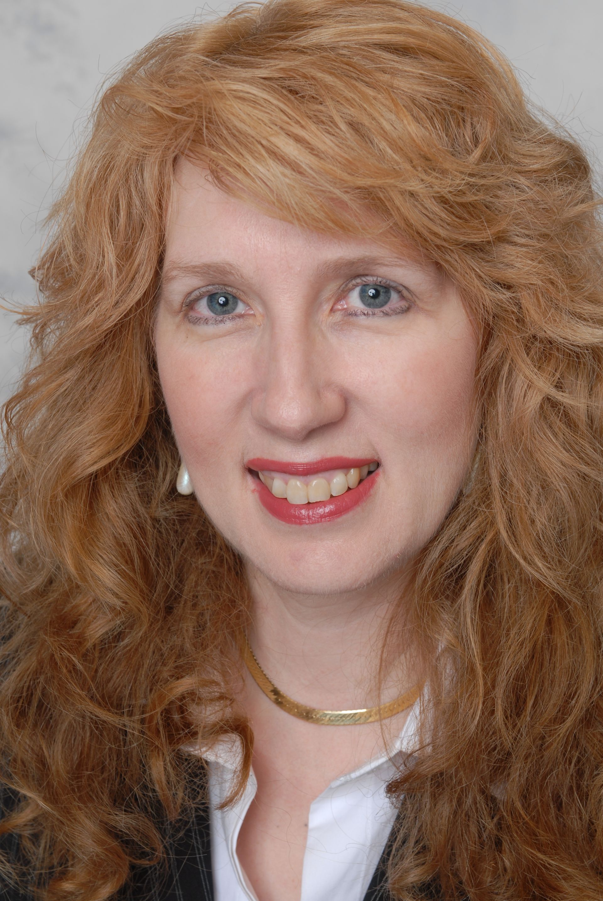A woman with long red hair and blue eyes is smiling for the camera.