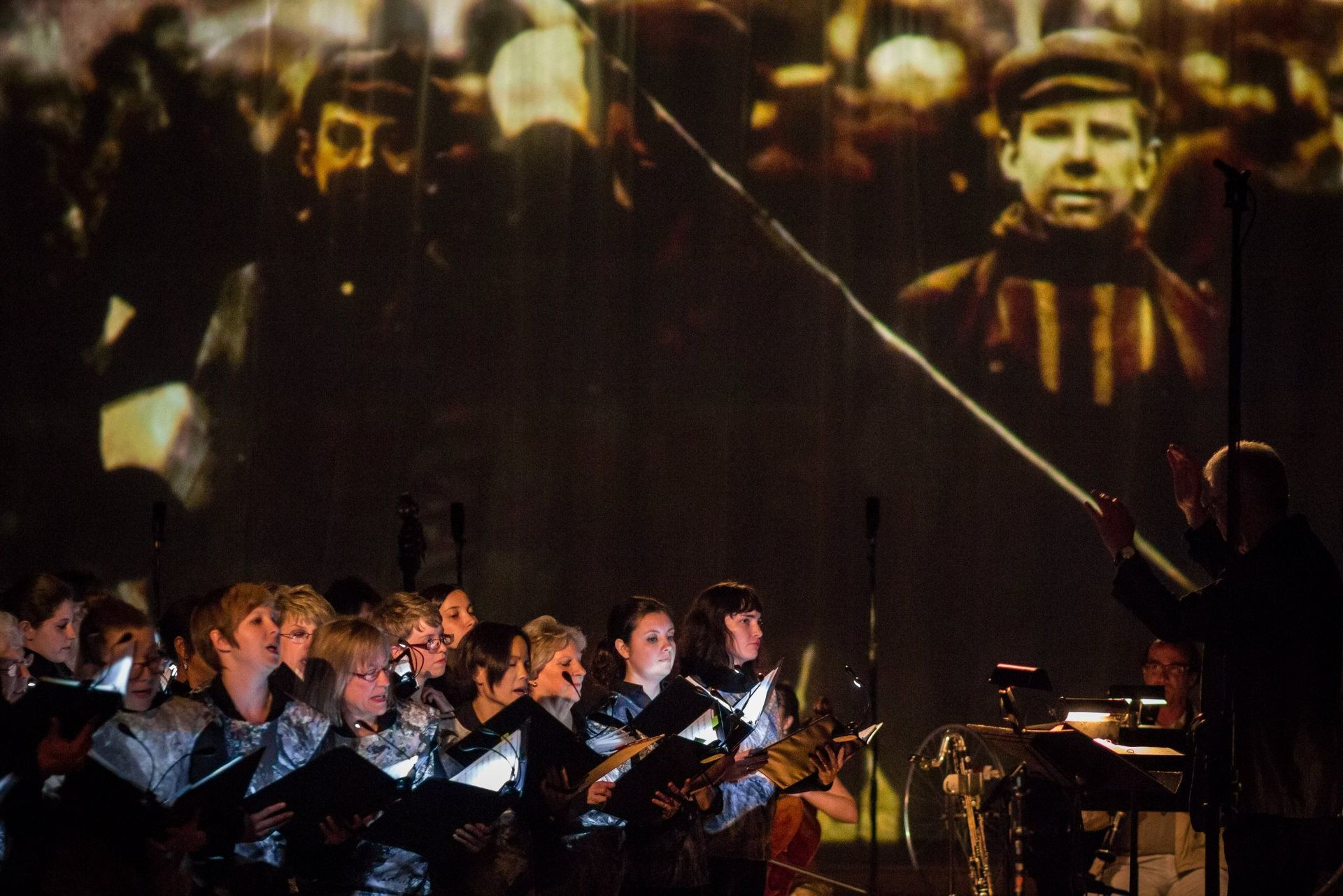 A choir is singing in front of a large screen with a picture of a man on it.