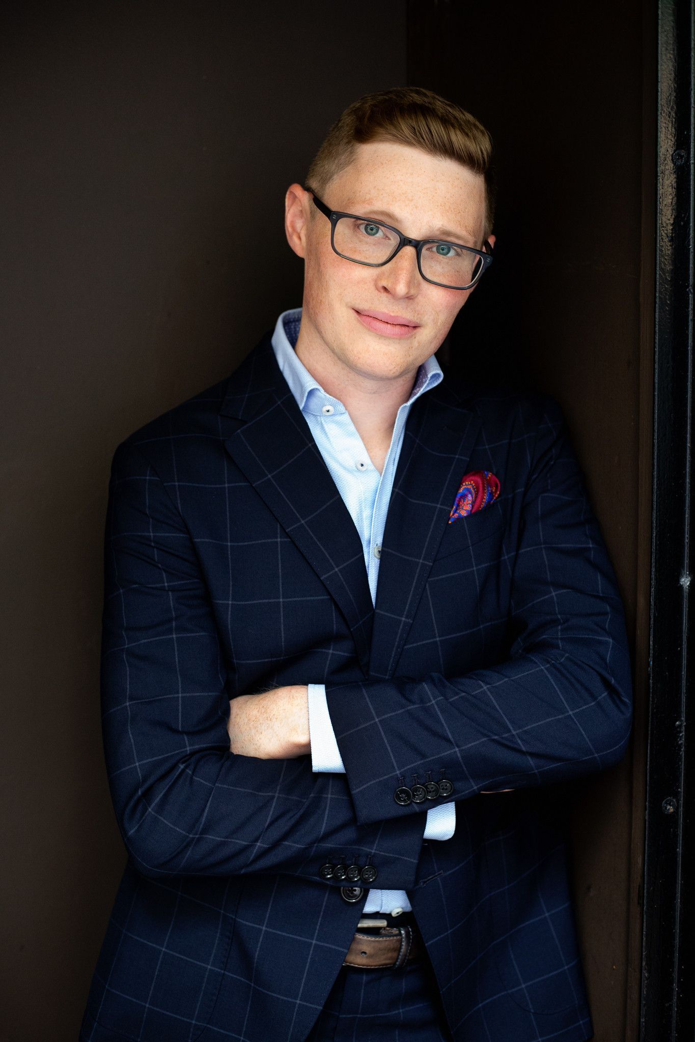 A man in a suit and glasses is standing with his arms crossed.