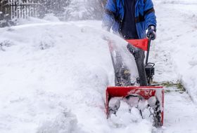 A snowplow plow clearing up snow from a sidewalk. 