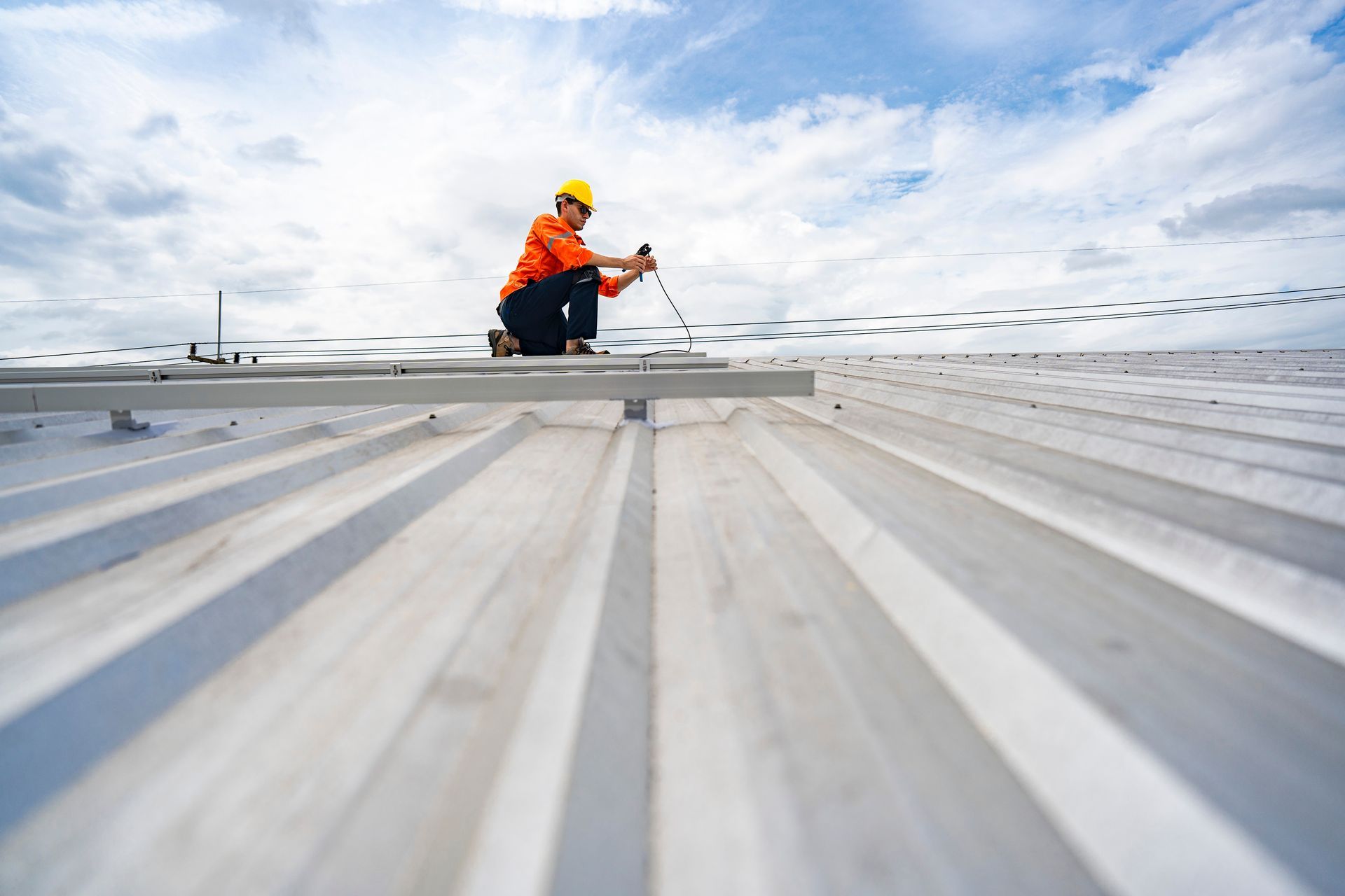 A worker is installing metal roofing panels using safety gear under a cloudy sky A worker is installing metal roofing panels using safety gear under a cloudy sky