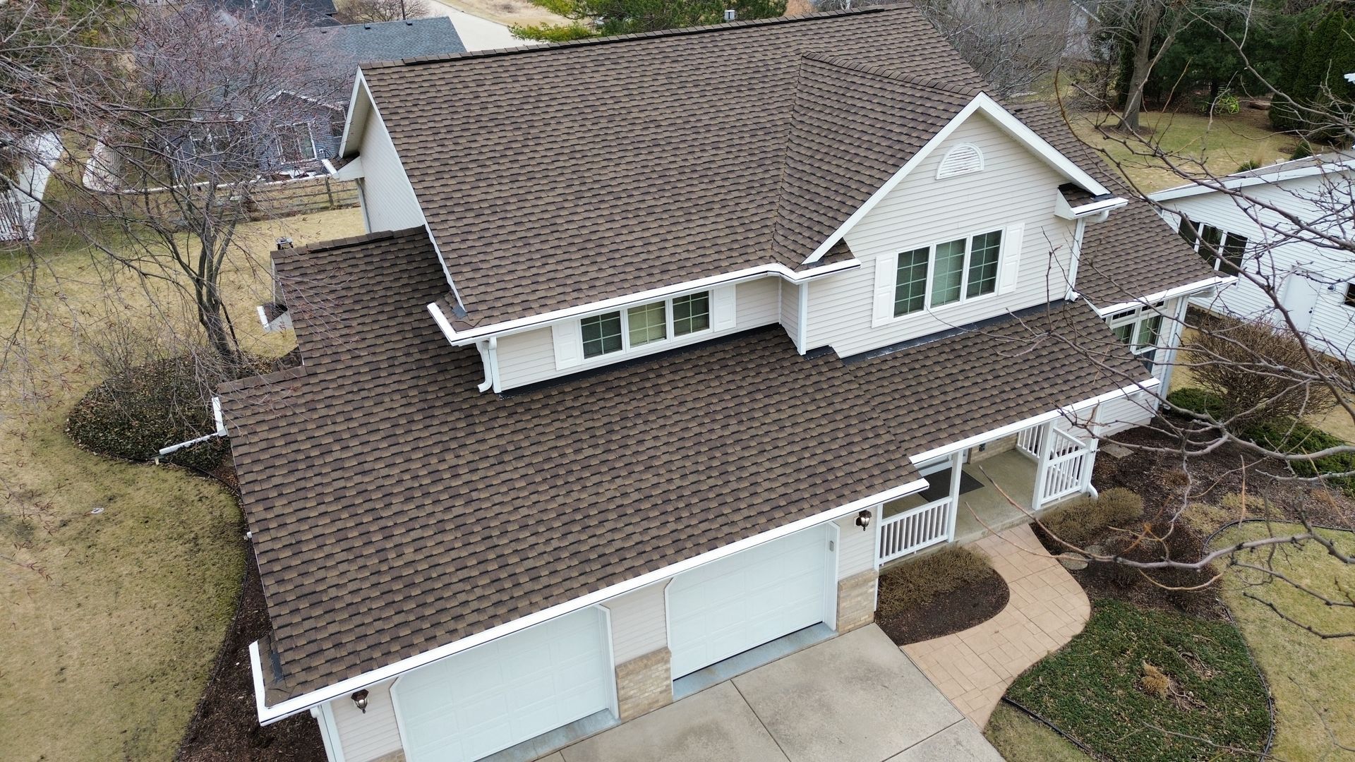 An elevated view of a two-story house with a brown shingled roof, a front-facing garage, and a winding walkway.