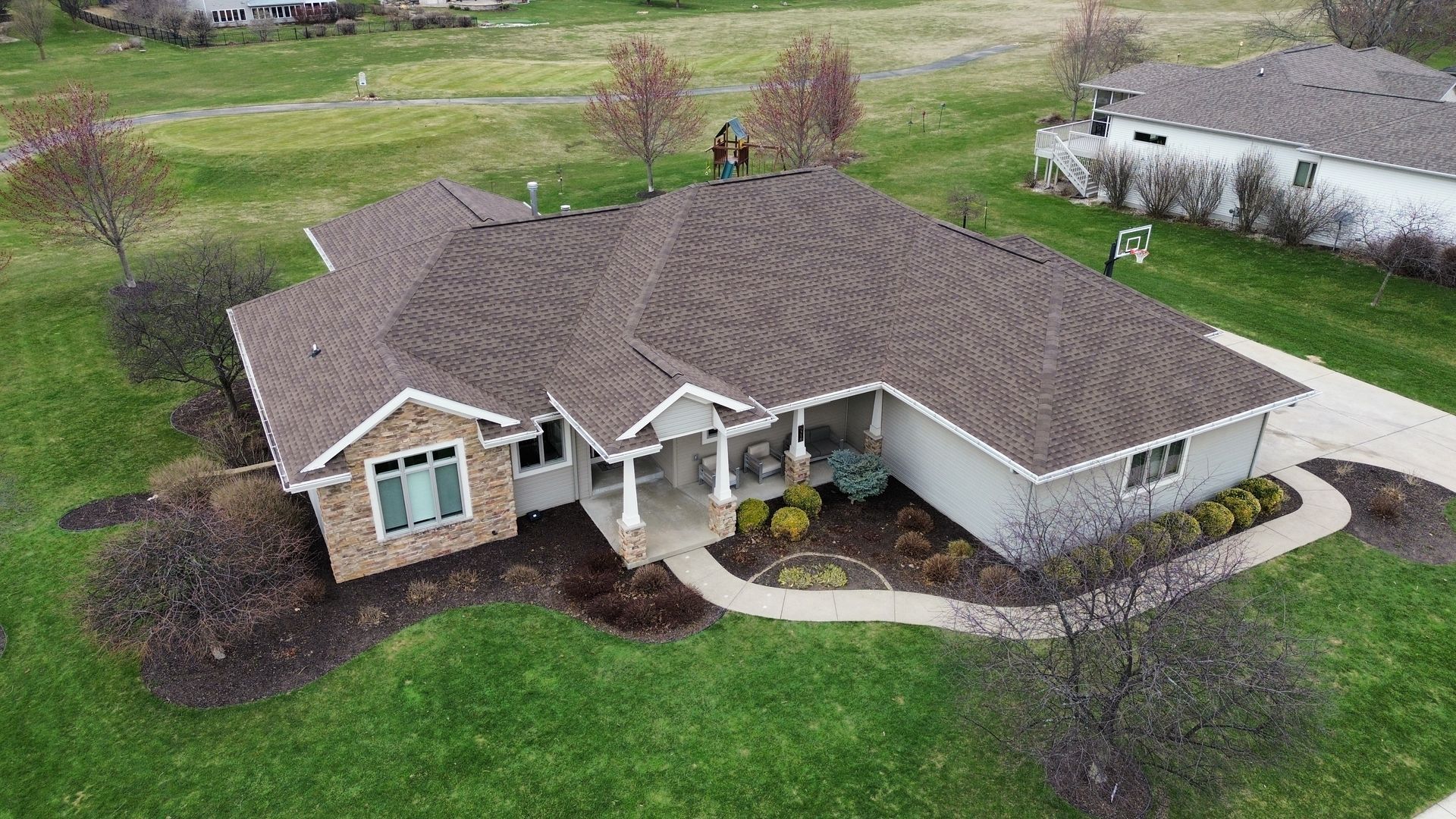 An aerial view of a single-story suburban house with a brown shingled roof, light siding, and a stone facade entrance.