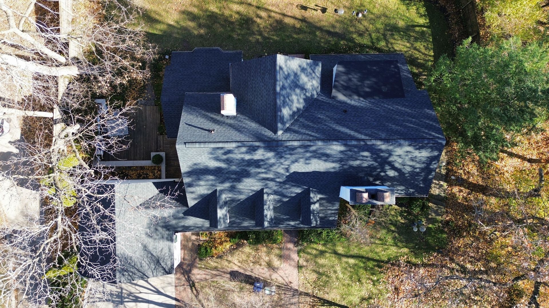Aerial view of a house roof surrounded by trees with shadows cast across the shingles.