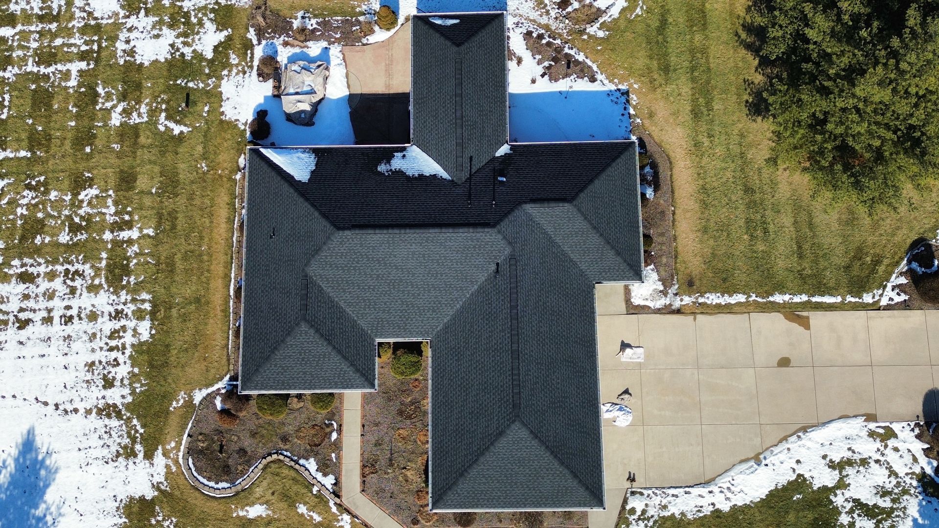 Aerial view of a residential house roof with sections of dark shingles and blue tarp covering an area under repair.