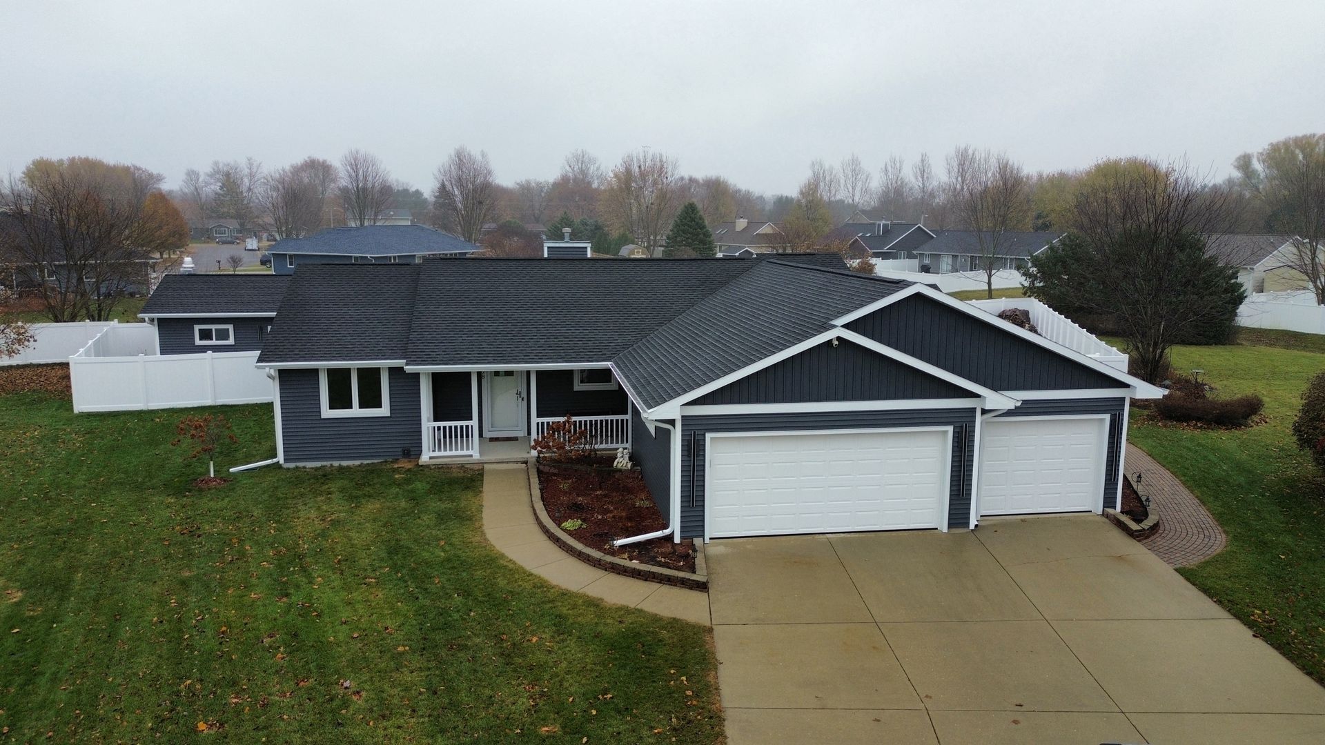 A single-story, dark blue house with a gray shingle roof, double garage, and white trim on an overcast day.
