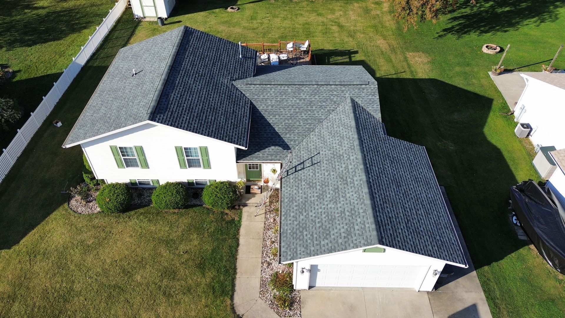 High-angle aerial view of a white, single-story house with a grey shingled roof, attached garage, and green lawn.