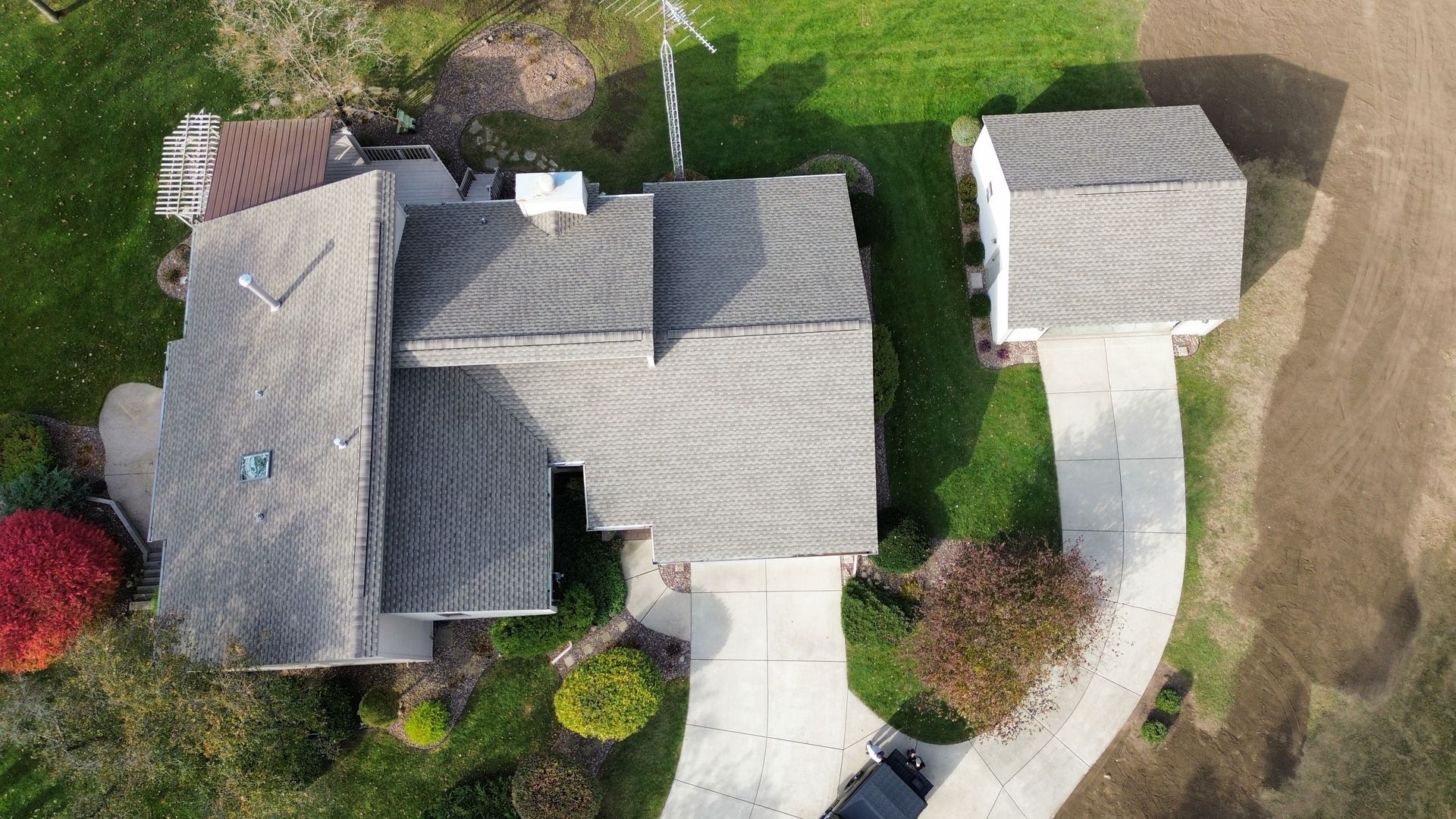 Aerial view of a residential house with a gray roof and attached garage, surrounded by green lawns and a paved driveway.
