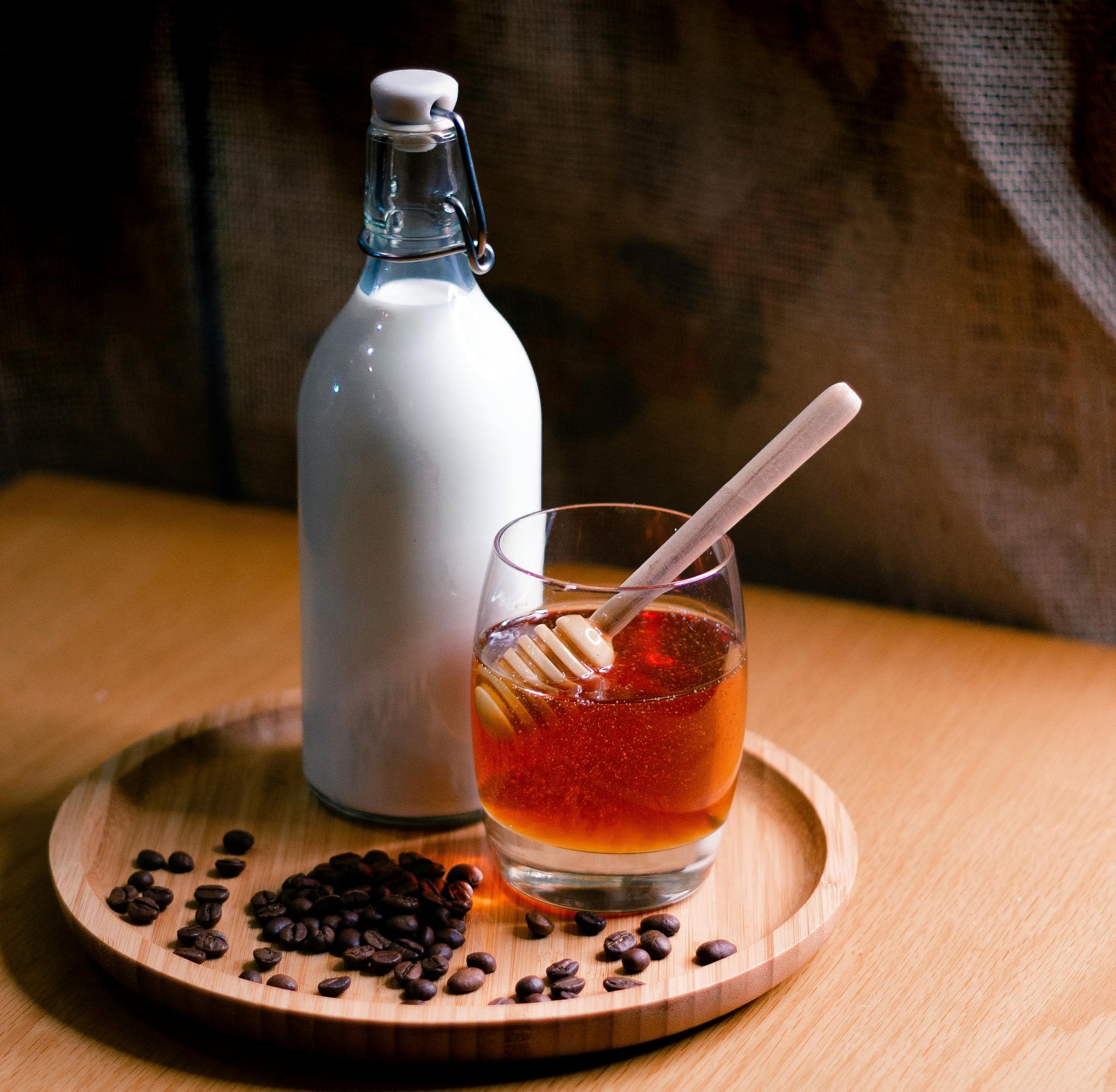 Bottle of milk, glass of honey, wooden honey dipper, coffee beans, all on a wooden tray.