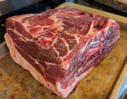 Raw beef roast with visible marbling and fat on a wooden cutting board.