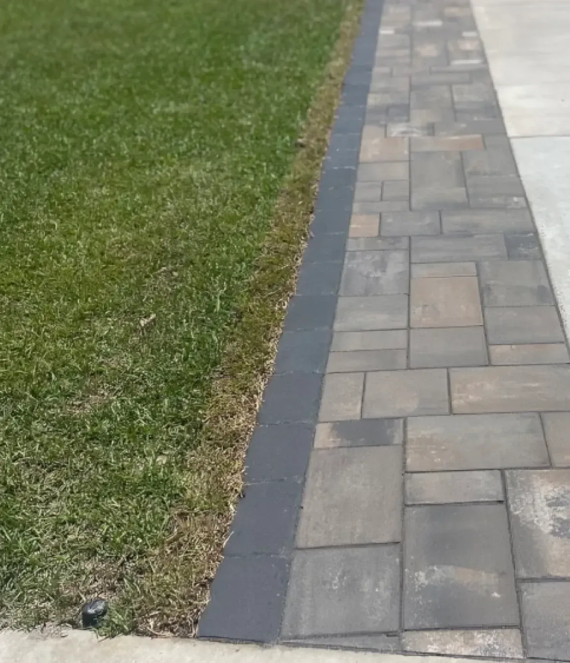 Paved walkway beside a green lawn, with gray pavers and a dark border